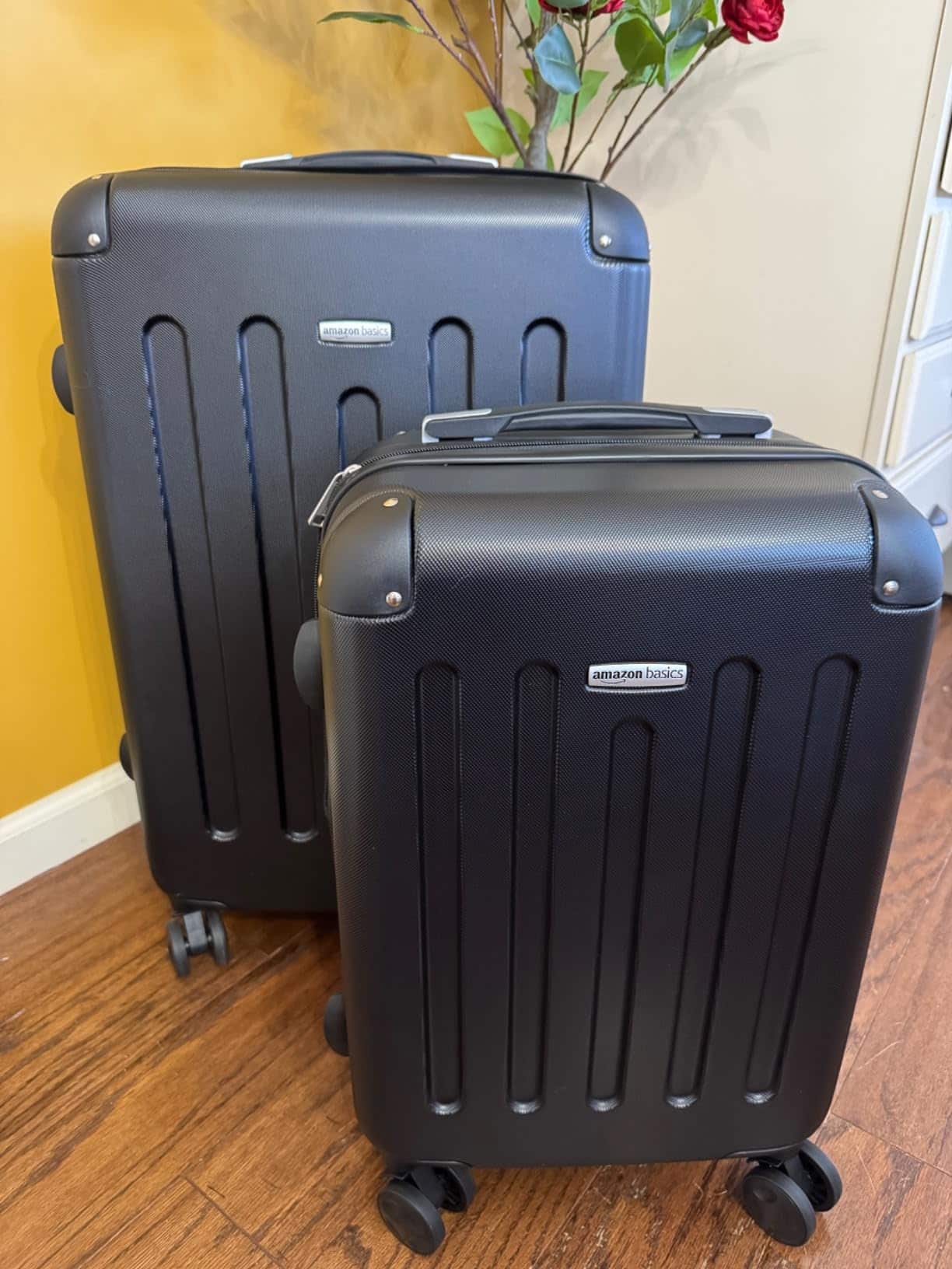 Two black Amazon Basics hardside suitcases standing on a wooden floor, showing the textured shell and spinner wheels.
