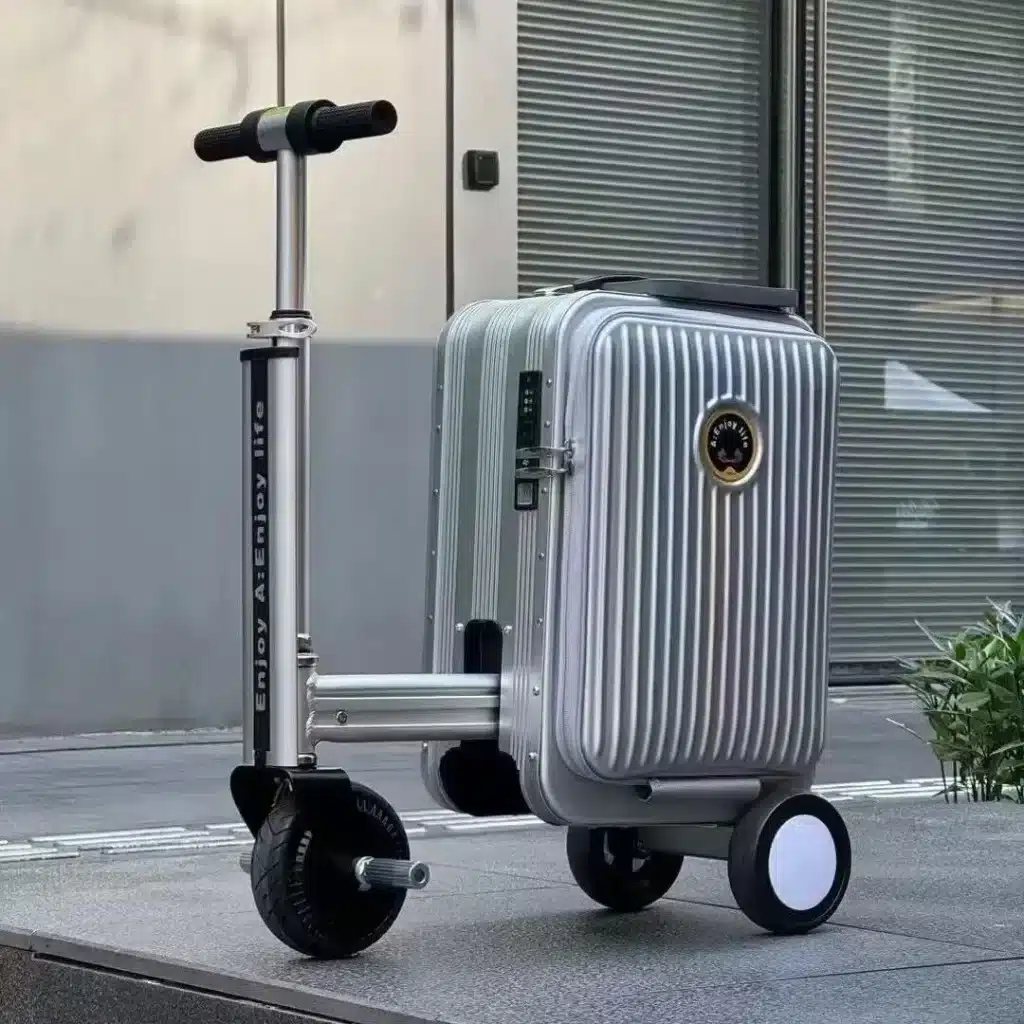Designer Rideable Electric Luggage Review (20-Inch) 5 Rideable electric luggage with foldable scooter handle and motorized front wheel, shown in silver on an outdoor pavement.