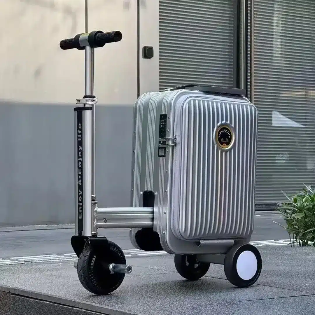 Rideable electric luggage with foldable scooter handle and motorized front wheel, shown in silver on an outdoor pavement.