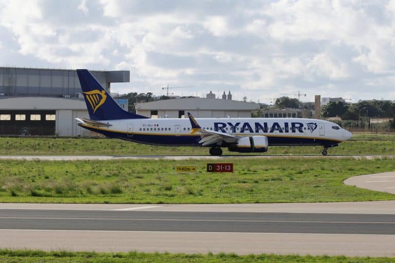 Ryanair Boeing 737 aircraft taxiing on the runway at an airport, with hangars and cloudy sky in the background.