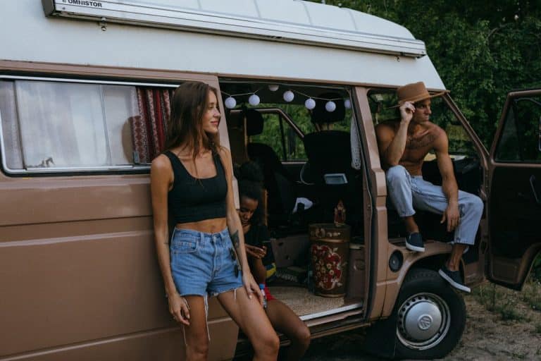 Three people relaxing beside a vintage camper van with the sliding door open, enjoying an outdoor RV stop in a natural setting.
