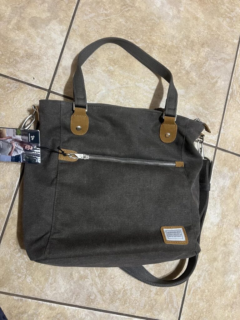 Travelon Anti-Theft Heritage Tote Bag in pewter cotton canvas with suede trim, front zip pocket, and dual handles displayed on tiled floor
