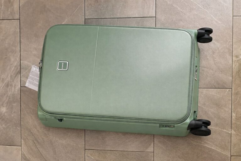 Hanke 28-inch expandable hard-shell checked luggage in sage green lying flat on a light gray tiled floor with four black spinner wheels and TSA lock visible.