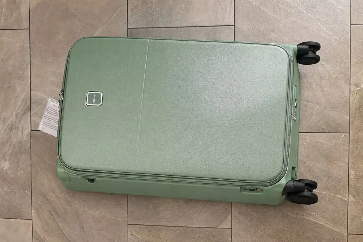 Hanke 28-inch expandable hard-shell checked luggage in sage green lying flat on a light gray tiled floor with four black spinner wheels and TSA lock visible.