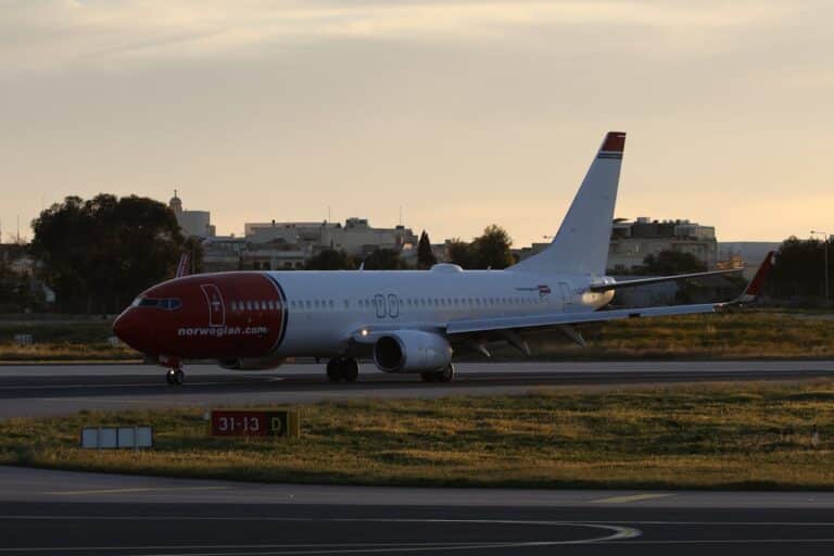 Norwegian Airlines Boeing 737 aircraft taxiing on the runway during golden hour at an airport.
