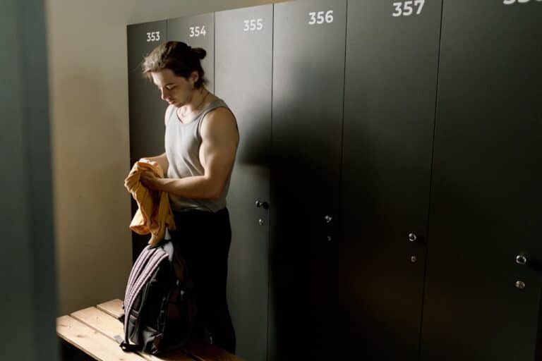 Man organizing gym clothes and backpack inside a modern gym locker room after a workout