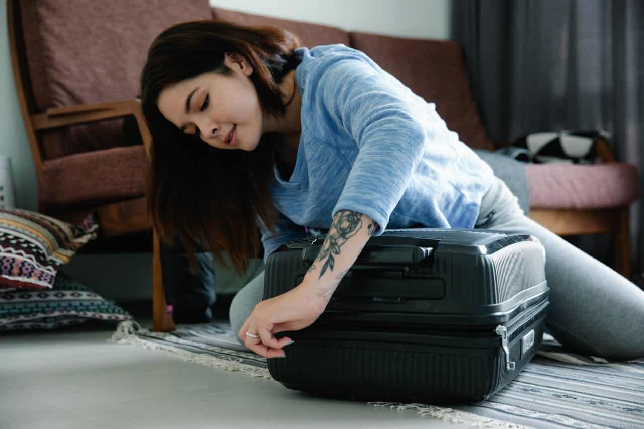 Woman packing a black hard shell suitcase on the floor at home before traveling to Southeast Asia