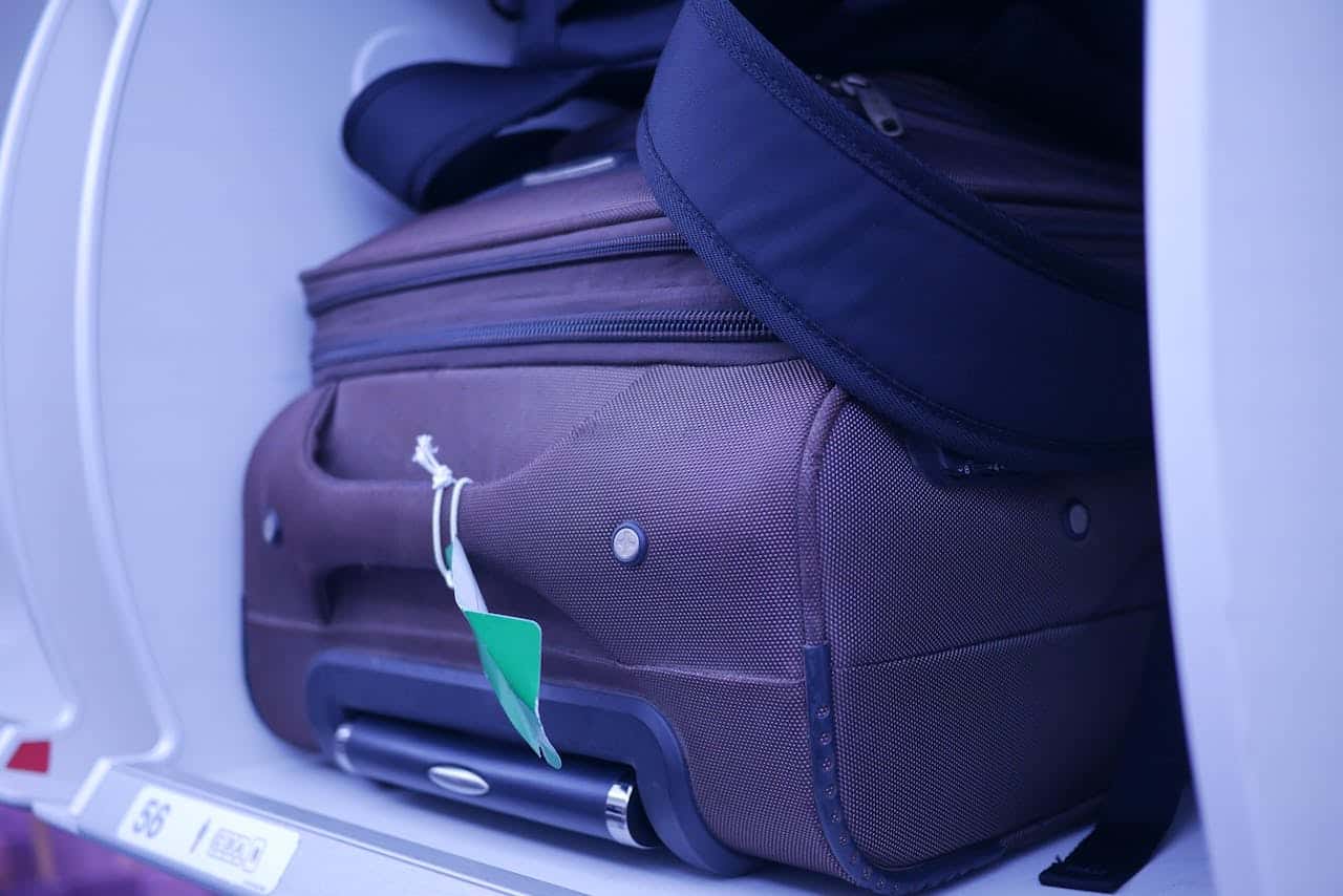 Lightweight cabin suitcase placed in an airplane overhead compartment with a travel bag on top