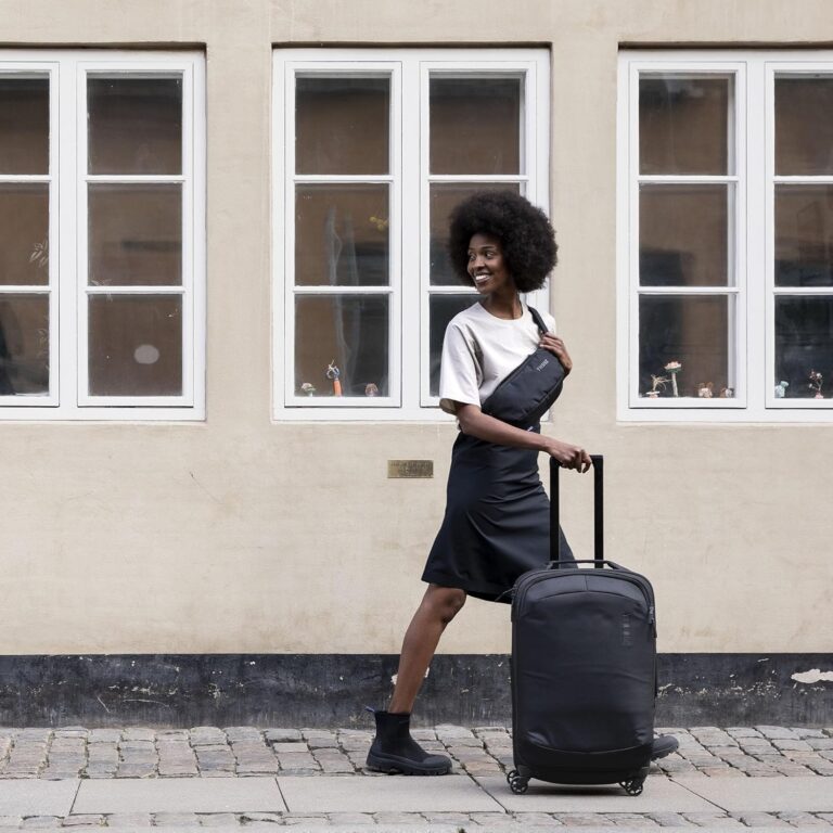 Woman walking with Thule Subterra checked spinner suitcase on cobblestone street, travel lifestyle luggage in use
