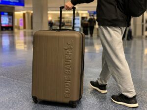 Traveler pulling a brown Eddie Bauer hard shell suitcase through an airport terminal with casual travel outfit and spinner wheels visible