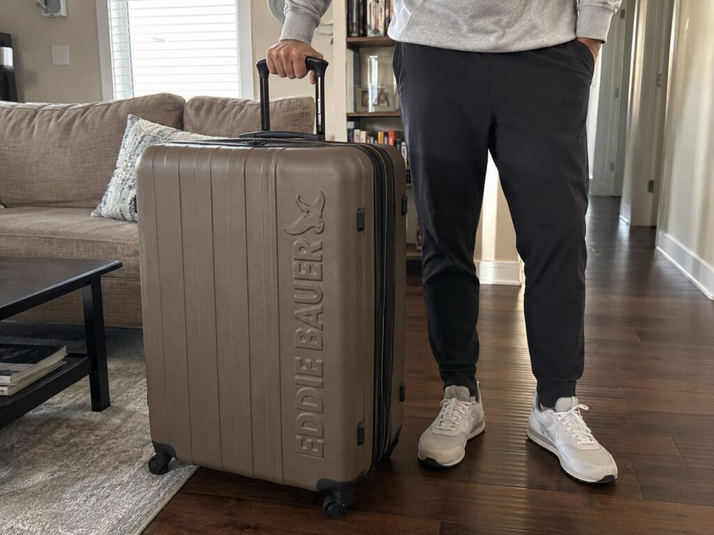 Eddie Bauer Flatiron Check-In Luggage Review 9 Traveler holding an Eddie Bauer Flatiron expandable hard shell suitcase in a modern living room before a trip