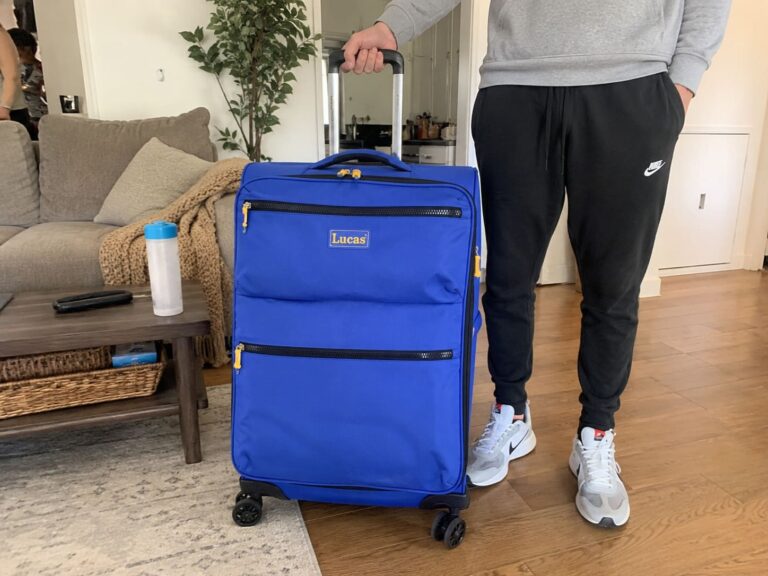 Person holding a blue Lucas softside spinner suitcase in a living room before travel, showing the lightweight design, telescopic handle, and smooth-rolling wheels.