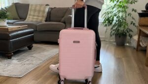 Person holding a pink Rockland Palm Beach hardside carry-on suitcase in a living room before travel