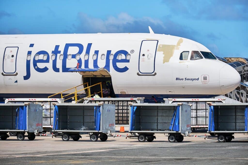 JetBlue airplane parked at the airport with luggage carts and baggage loading equipment on the tarmac