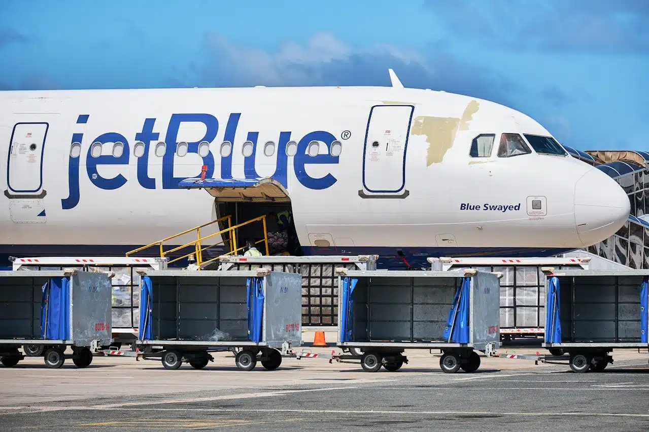 JetBlue airplane parked at the airport with luggage carts and baggage loading equipment on the tarmac