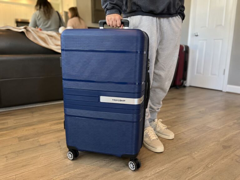 Traveler holding a navy blue Tripcomp hard-shell suitcase in a living room, showcasing the lightweight spinner luggage design and telescoping handle.