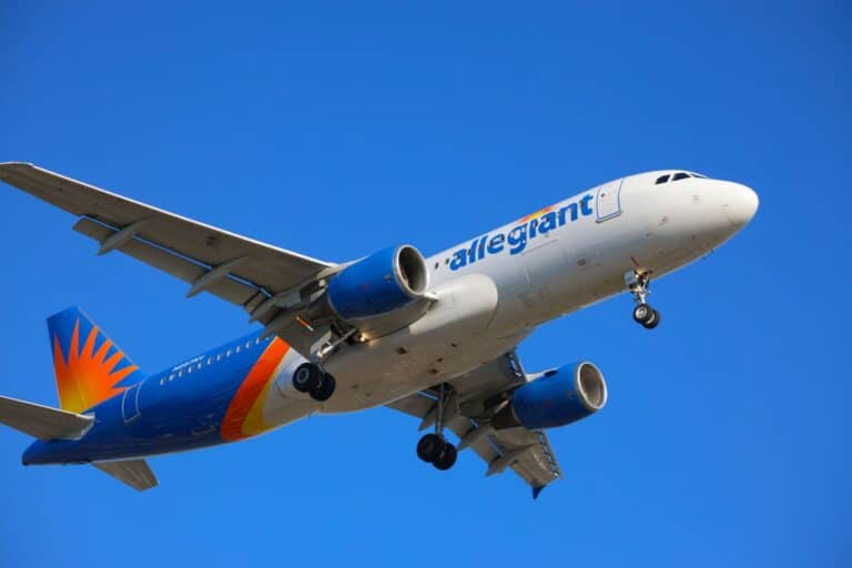 Allegiant Air passenger plane flying against a clear blue sky with its landing gear extended.