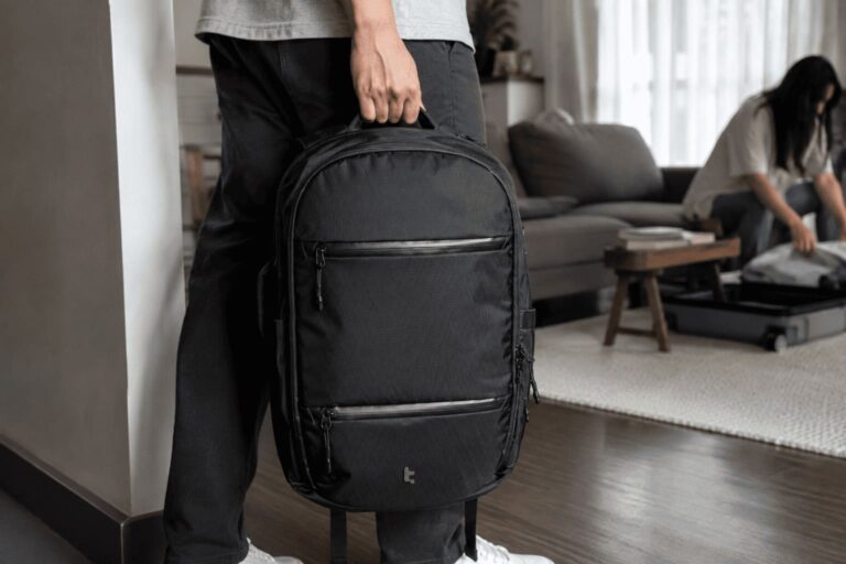 Person holding a black tomtoc UrbanEX-T77 26L laptop backpack while preparing for a trip in a living room.